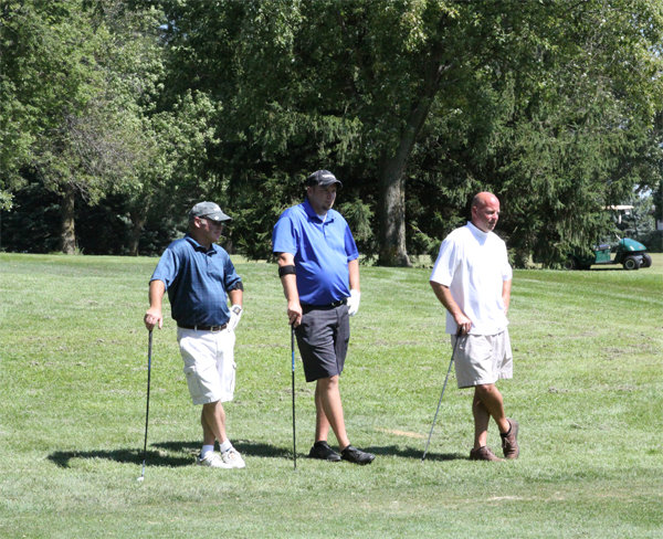 Three men lean on their golf clubs and pose for a photo together