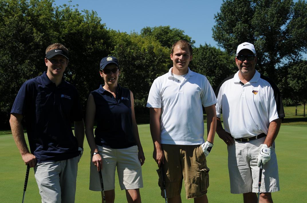 Four people in golf gear pose on the golf course for a photo