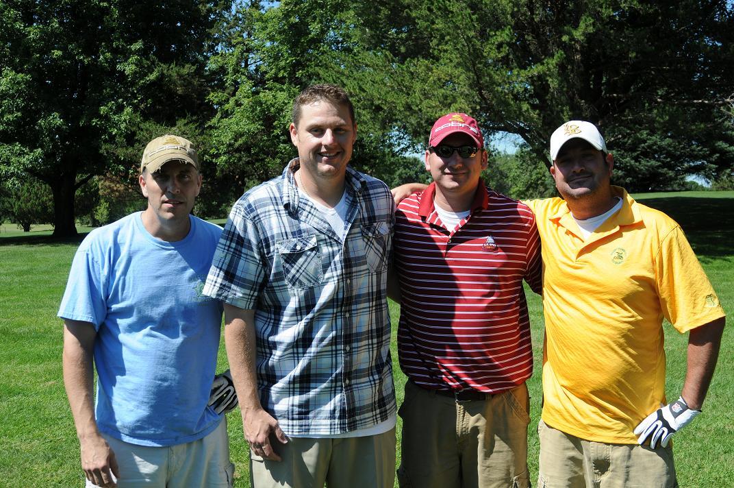 Four men link arms and pose for a photo on the golf course together