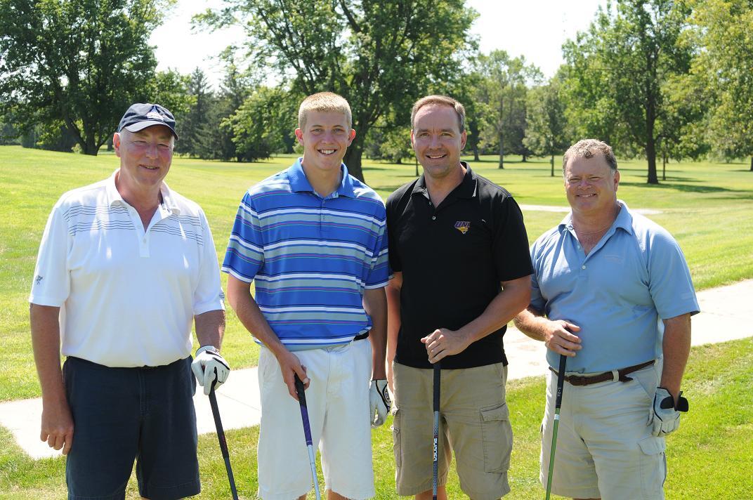 Four men pose with golf clubs on the golf course for a group photo