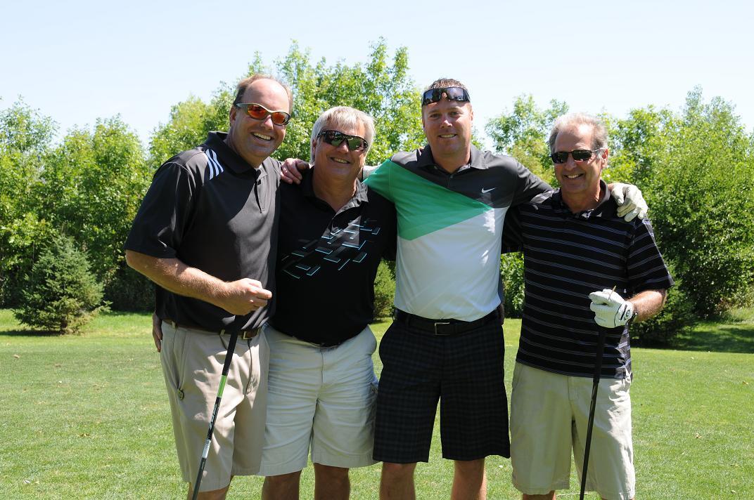 Four people with their arms linked on the golf course smile for a photo