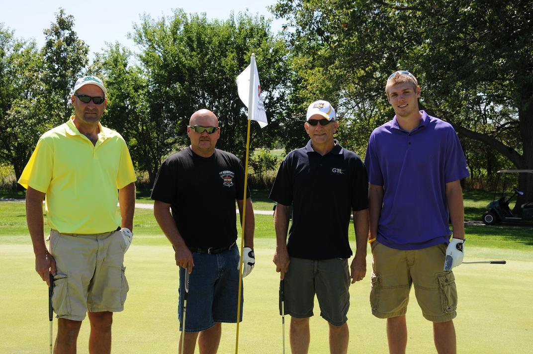 Four men posing with golf clubs at the golf course