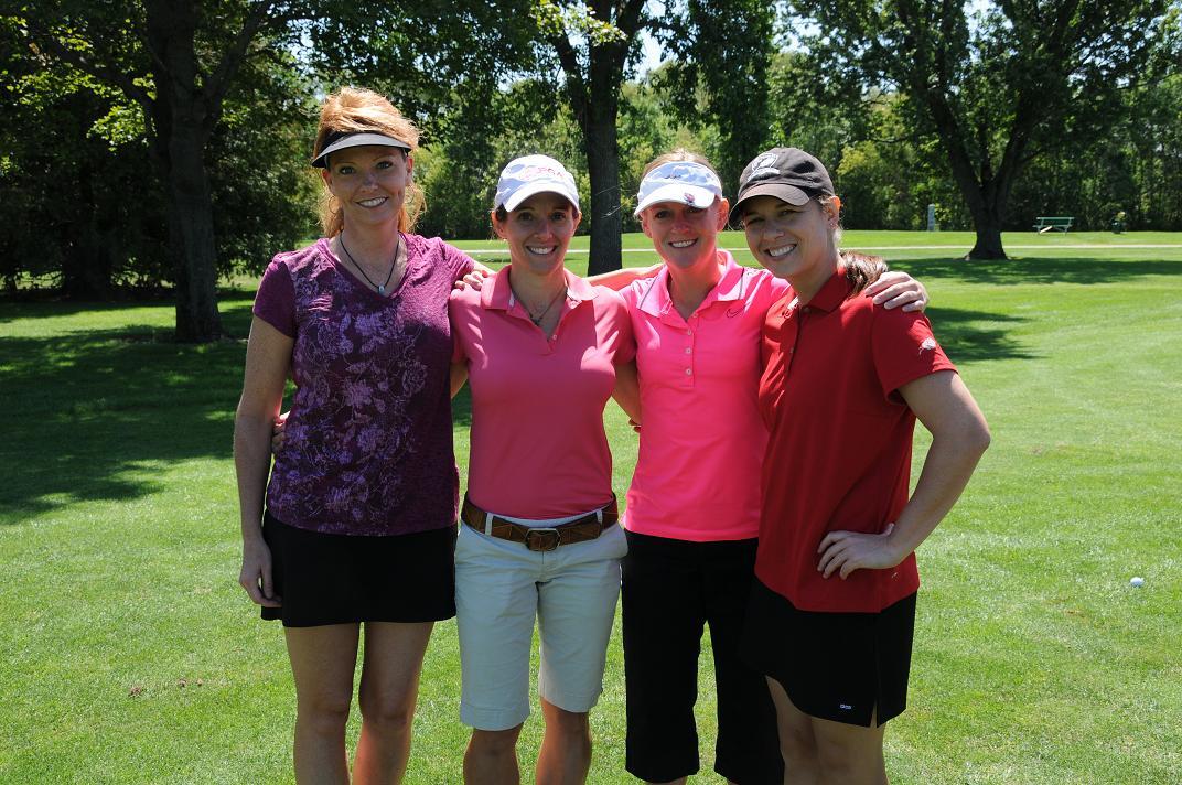 Four women smile and pose for a photo on the golf course