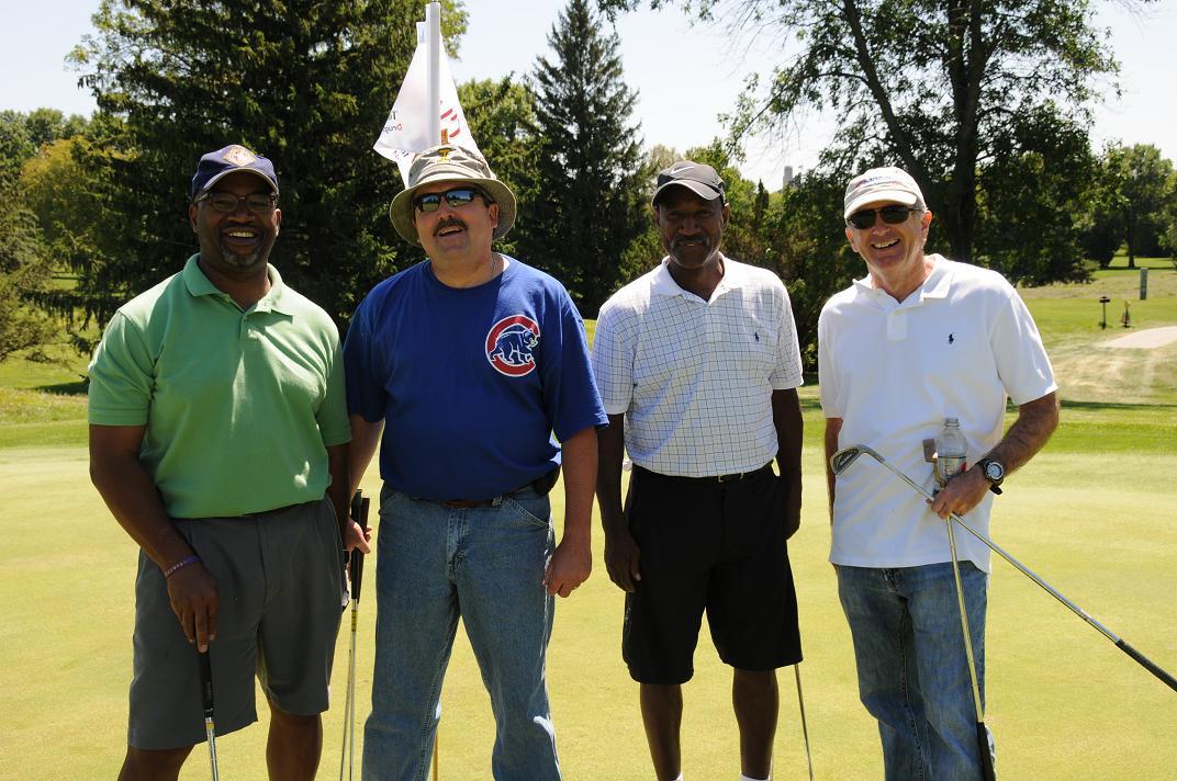 Men standing in a group and smiling for a photo on the golf course