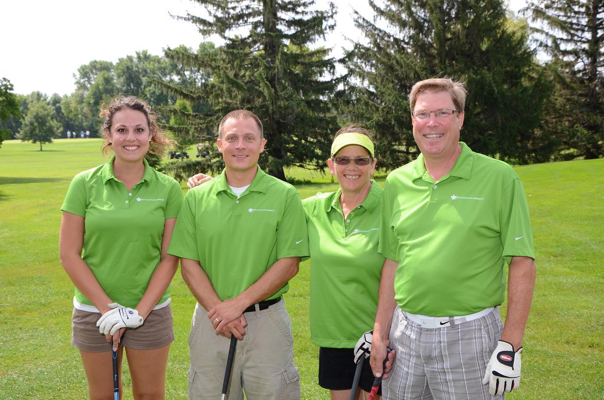 Four people in green polos pose for a photo on the golf course