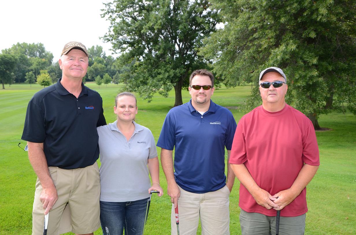 Four individuals on the golf course pose for group photo