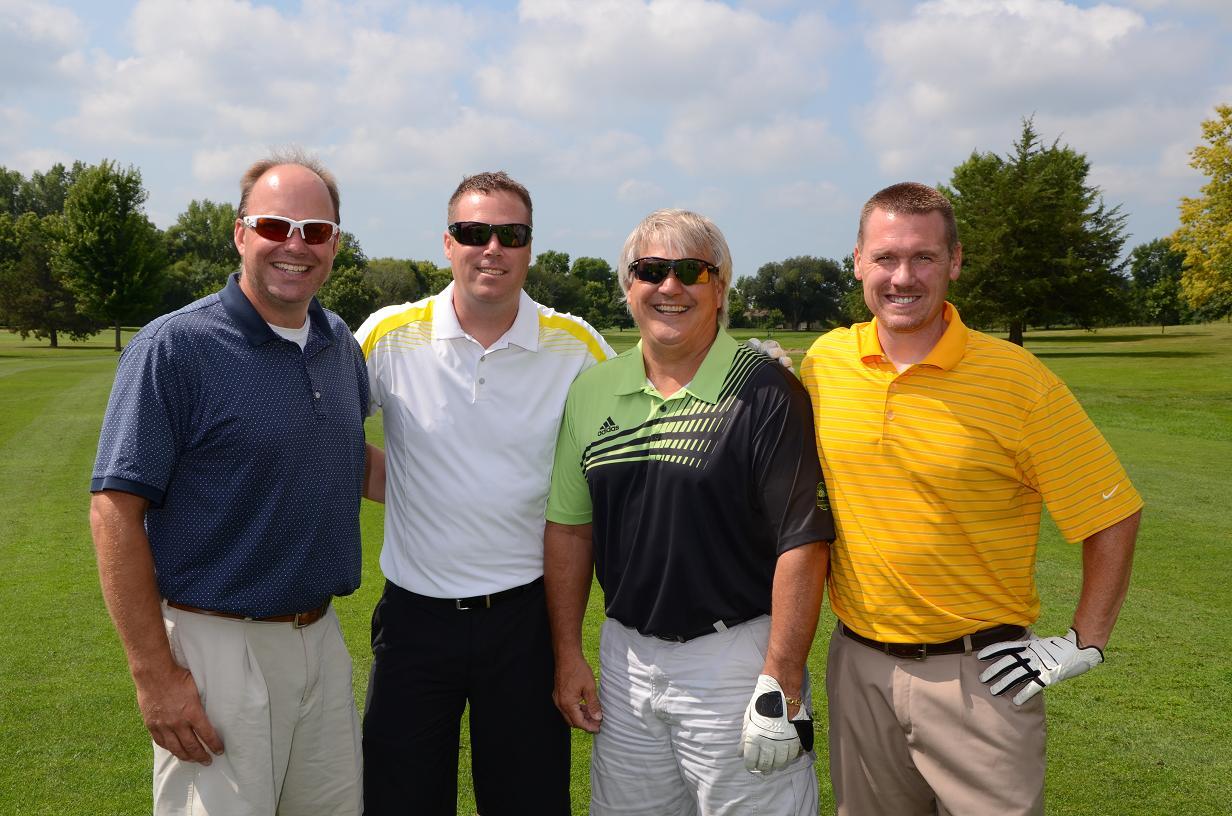 Four men smile for a photo on the golf course