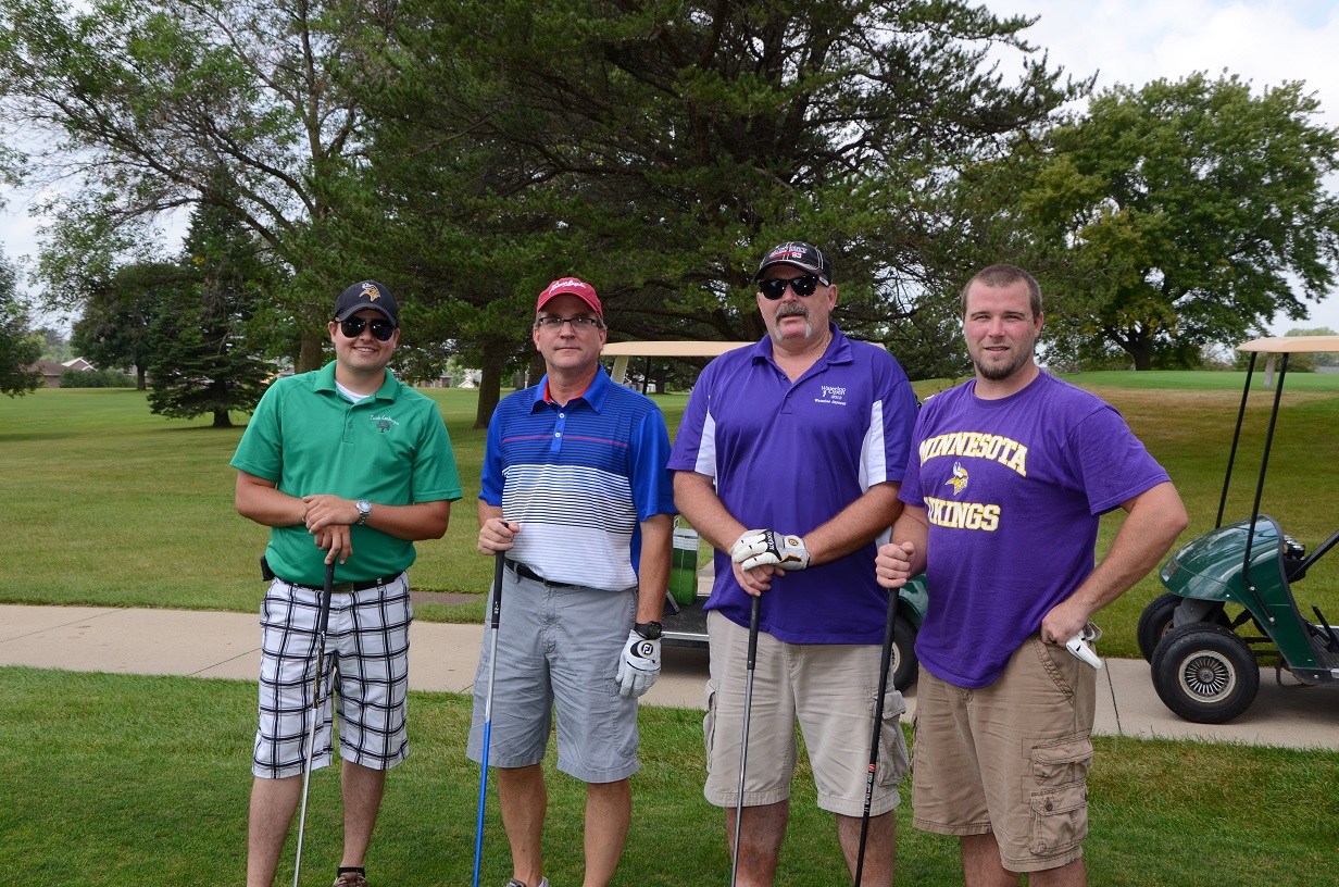 Golfers with golf clubs pose for a picture.