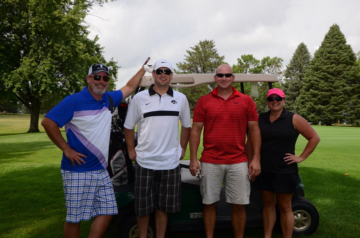 Four people pose for photo in front of golf cart