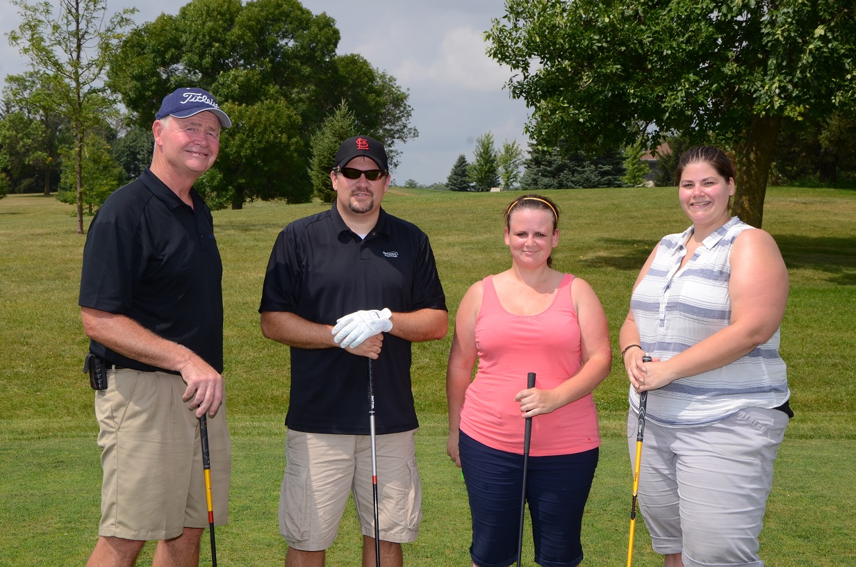 Four people pose with their golf clubs outdoors