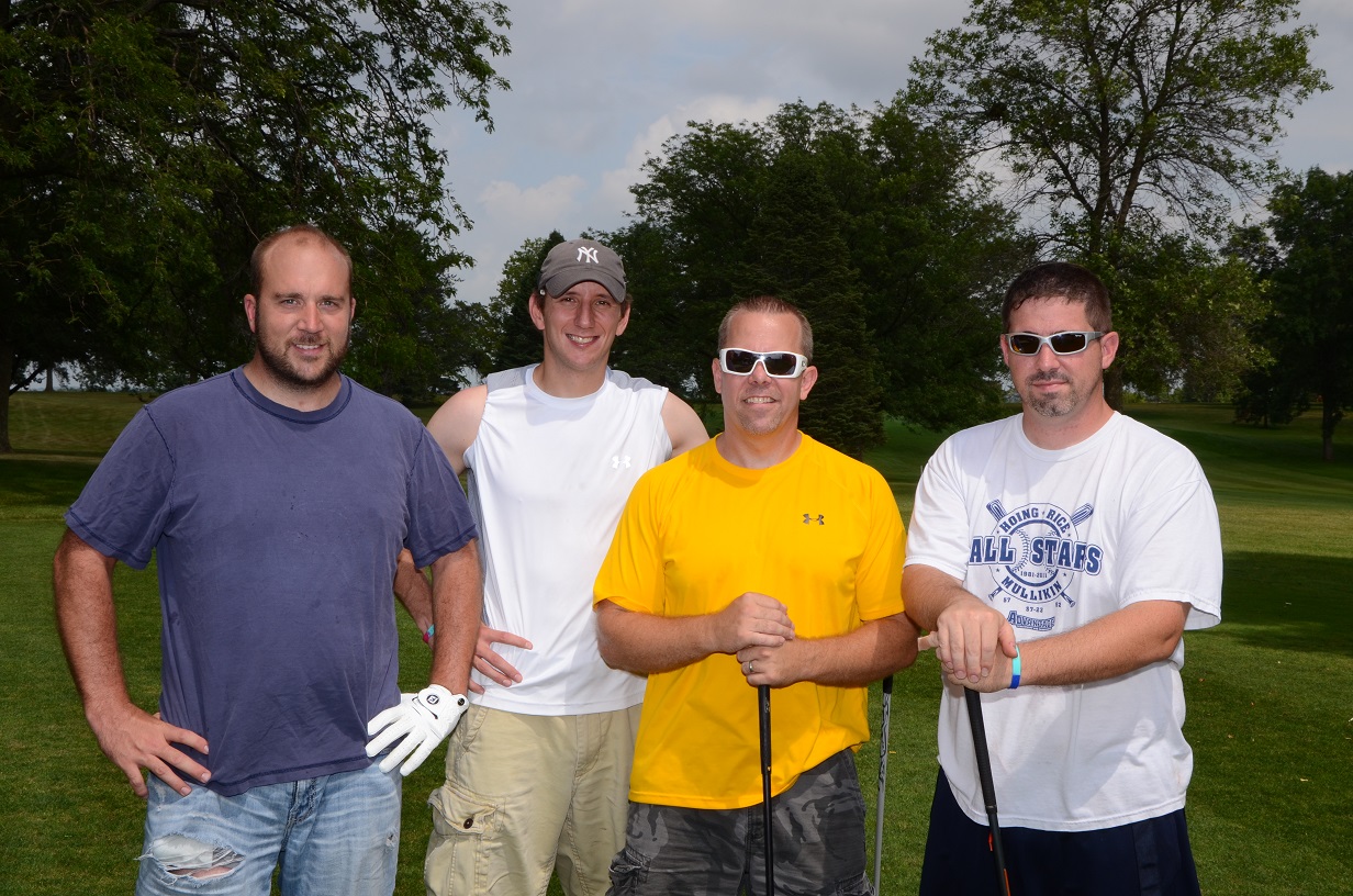 Four men pose outside for a photo on the golf course