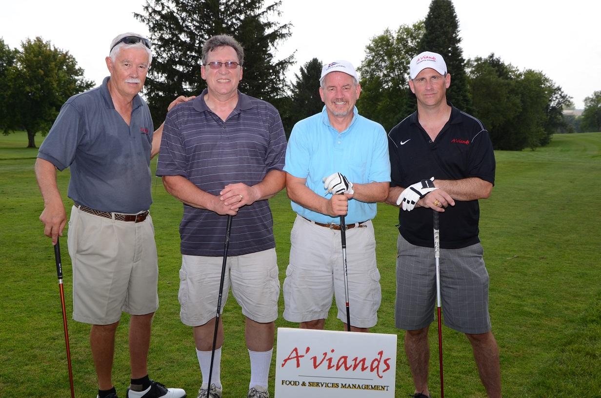 Men with golf clubs on the course pose for a photo