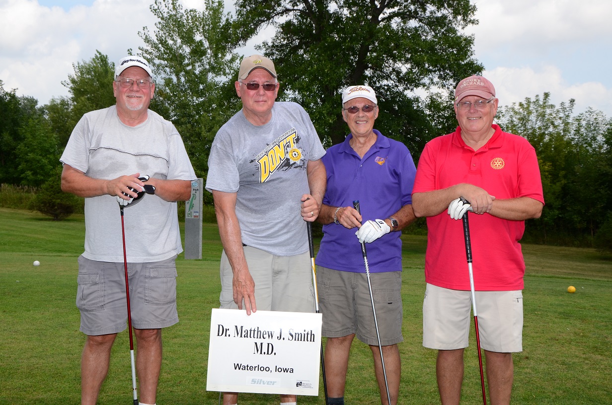 Four people with golf clubs are posing for a photo outside