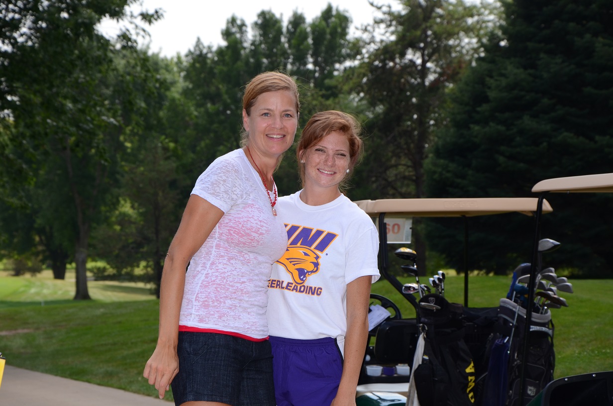 Two women pose for a photo by golf cart